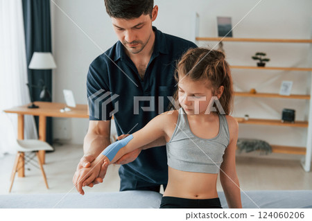 Professional physiotherapist putting kinesio tape on kid arms in clinic Professional physiotherapist putting kinesio tape on kid arms in clinic 124060206