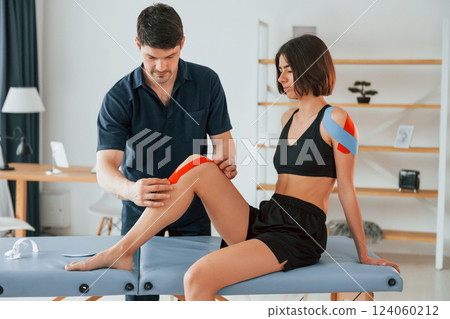 Working with legs. Woman visiting physiologist that putting kinesio tape on the skin 124060212
