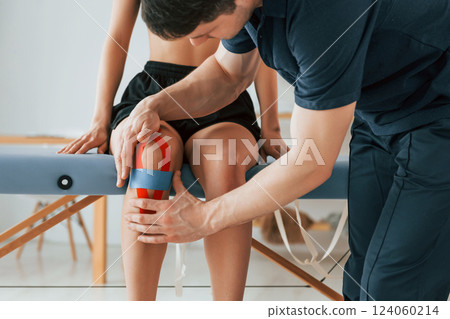 Working with legs. Woman visiting physiologist that putting kinesio tape on the skin Working with legs. Woman visiting physiologist that putting kinesio tape on the skin 124060214