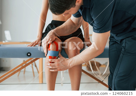 Working with legs. Woman visiting physiologist that putting kinesio tape on the skin 124060215