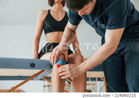 Almost finishing the legs. Woman visiting physiologist that putting kinesio tape on the skin Almost finishing the legs. Woman visiting physiologist that putting kinesio tape on the skin 124060218