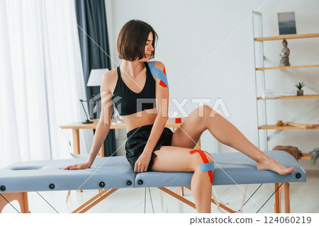 Sitting on the table. Woman with kinesio tape is in the clinic indoors 124060219