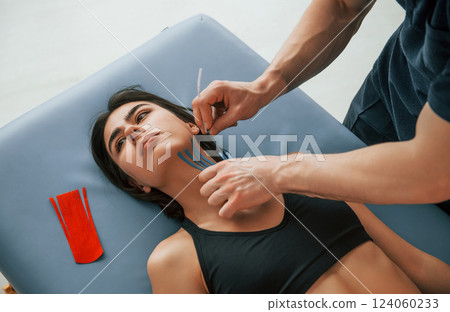 Laying down on the table. Woman visiting physiologist that putting kinesio tape on the skin Laying down on the table. Woman visiting physiologist that putting kinesio tape on the skin 124060233