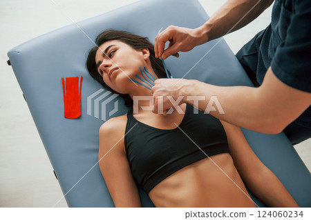 Laying down on the table. Woman visiting physiologist that putting kinesio tape on the skin 124060234