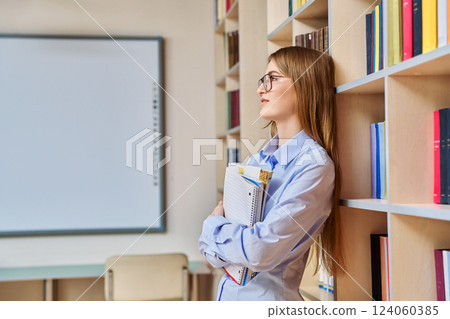 Portrait of student teenager girl holding textbooks inside classroom library 124060385