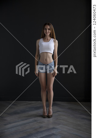 young girl in a t-shirt and shorts on a dark background, full length studio shot young girl in a t-shirt and shorts on a dark background, full length studio shot 124060473