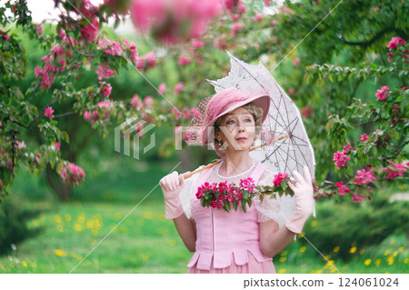 Happy natural adult mature woman of 60 years old in 18th century style pink hat, retro dress, gloves and umbrella in blossoming white apple orchard on summer day Happy natural adult mature woman of 60 years old in 18th century style pink hat, retro dress, gloves and umbrella in blossoming white apple orchard on summer day 124061024