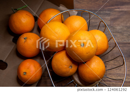 ripe unpeeled oranges in a fruit basket on a brown wooden table. 124061292