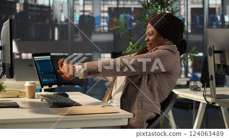Woman CEO suffers from muscle cramps due to incorrect posture at the desk, dealing with neck and back ache while he solves tasks at workstation. Director with spasm and sedentary life. Camera A. 124063489