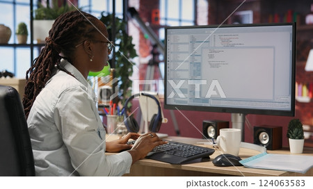 Engineer in home office looks at UI on computer monitor, typing and executing programming code. Panning shot of IT worker using coding application to write and test code in modern apartment, camera B 124063583
