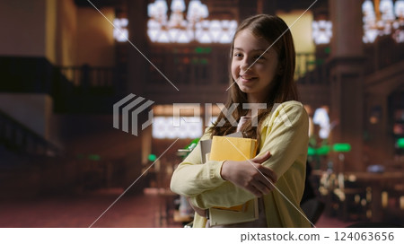 Portrait of sweet preadolescent carrying her books and class notes in the library, preparing for an intense studying session with her textbooks. Academic environment to ensure development. Camera B. 124063656