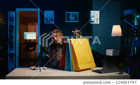 Girl holding colorful shopping bags in hand, showing subscribers purchases she recently got. Content creator presenting fanbase new acquisitions, filming herself in apartment, camera B Girl holding colorful shopping bags in hand, showing subscribers purchases she recently got. Content creator presenting fanbase new acquisitions, filming herself in apartment, camera B 124063747