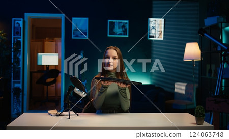 Young entertainer presenting sleek laptop from brand sponsoring video, urging viewers to purchase it. Girl does influencer marketing by advertising thin notebook to audience in studio, camera B 124063748