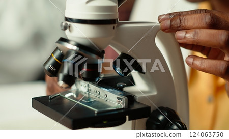 African american scholar studies medical science in a college library, doing research on viruses using a microscope. Girl works on exam preparation for success in a scientific career. Camera B. African american scholar studies medical science in a college library, doing research on viruses using a microscope. Girl works on exam preparation for success in a scientific career. Camera B. 124063750