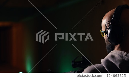 Man in firing range doing shooting activity with rifle, wearing earmuffs to protect hearing. Person training with semiautomatic weapon, using safety gear to prevent damage from gunshots, camera B Man in firing range doing shooting activity with rifle, wearing earmuffs to protect hearing. Person training with semiautomatic weapon, using safety gear to prevent damage from gunshots, camera B 124063825