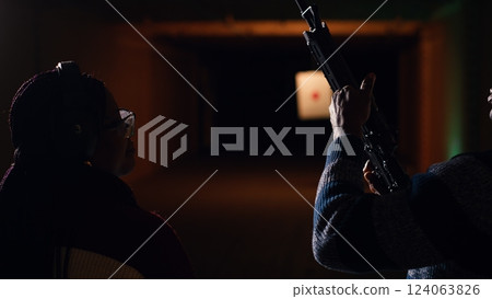 Man holds rifle, enjoying recreational shooting experience in firing range next to group of friends. People practicing with weapons in safe environment at shooting range company, camera B Man holds rifle, enjoying recreational shooting experience in firing range next to group of friends. People practicing with weapons in safe environment at shooting range company, camera B 124063826