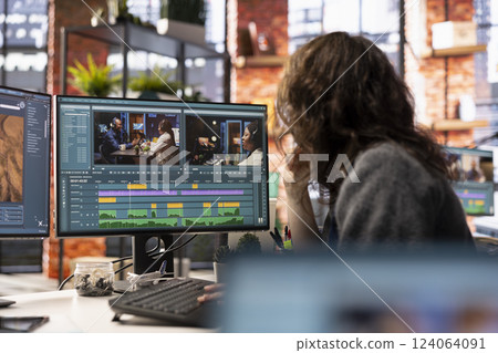 Video creator woman editing a music video on dual monitors in agency studio, multitasking between timeline editing and color grading. Professional editor uses tech tools and software. 124064091