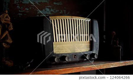 An antique radio with analog controls sits on a wooden shelf 124064266