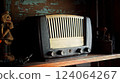 An antique radio with analog controls sits on a wooden shelf 124064267
