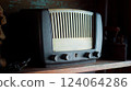 An antique radio with analog controls sits on a wooden shelf 124064286