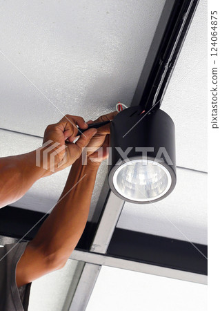Hands of an electrician installing a light on the ceiling. 124064875