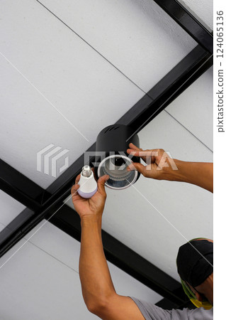 Hands of an electrician installing a light on the ceiling. Hands of an electrician installing a light on the ceiling. 124065136