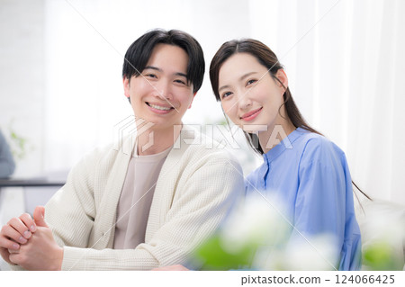 A newlywed couple relaxing in the living room, looking at the camera with a refreshing smile A newlywed couple relaxing in the living room, looking at the camera with a refreshing smile 124066425