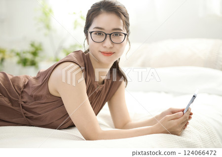 Young woman relaxing in bed and looking at her smartphone 124066472