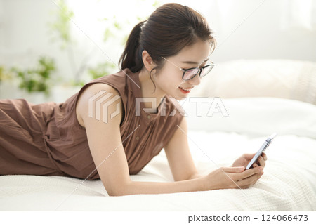 Young woman relaxing in bed and looking at her smartphone Young woman relaxing in bed and looking at her smartphone 124066473