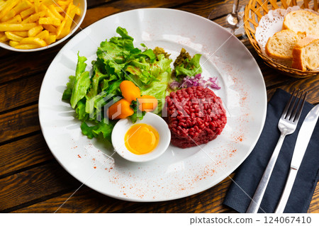 Tartar beef with quail egg and arugula served on plate. Modern French cuisine Tartar beef with quail egg and arugula served on plate. Modern French cuisine 124067410