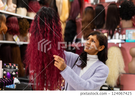 Hispanic woman choosing wigs from natural hair in specialized store Hispanic woman choosing wigs from natural hair in specialized store 124067425