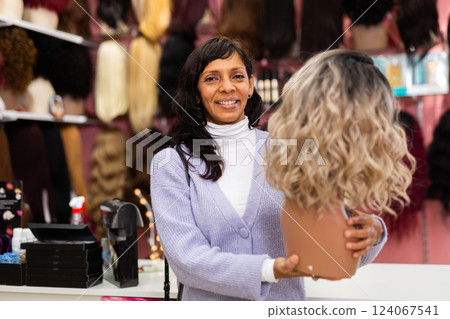 Latin american woman choosing natural hair wig at specialty boutique Latin american woman choosing natural hair wig at specialty boutique 124067541