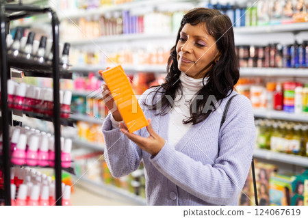 Hispanic woman choosing hair care treatments in cosmetics store Hispanic woman choosing hair care treatments in cosmetics store 124067619