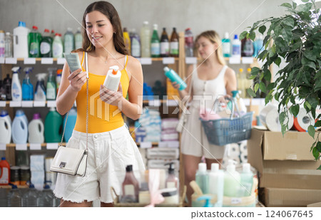 Woman consumer choose tanning product or sunscreen in household supermarket, while in background shoppers browse products Woman consumer choose tanning product or sunscreen in household supermarket, while in background shoppers browse products 124067645