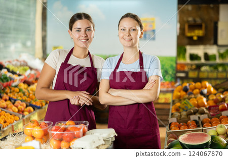 Happy two female sellers wearing apron and standing next to organic foods in supermarket Happy two female sellers wearing apron and standing next to organic foods in supermarket 124067870