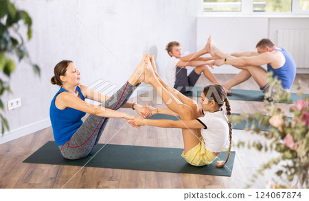Friendly sporty parents with preteen daughter and son touching each other feet and palms on gymnastic mats barefoot in yoga studio. Family health concept Friendly sporty parents with preteen daughter and son touching each other feet and palms on gymnastic mats barefoot in yoga studio. Family health concept 124067874