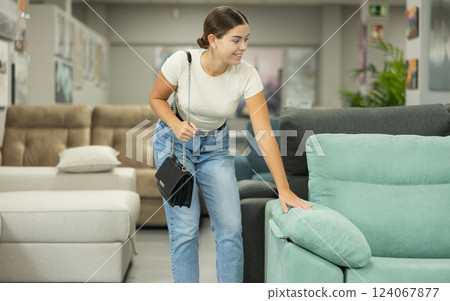 Girl in store inspects upholstered furniture. 124067877