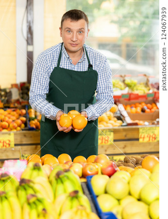 Friendly salesman offering ripe oranges in fruits and vegetables store 124067939