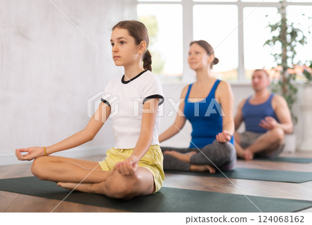 Teenage girl with her parents practices yoga in lotus position Teenage girl with her parents practices yoga in lotus position 124068162