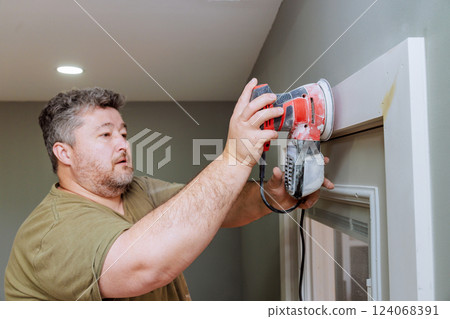Carpenter operates sander while preparing interior door molding surfaces for fresh paint job. Carpenter operates sander while preparing interior door molding surfaces for fresh paint job. 124068391