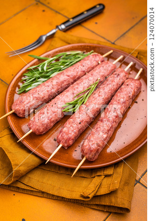 Raw Turkish Urfa kebab skewers on a plate with herbs. orange background. top view 124070014