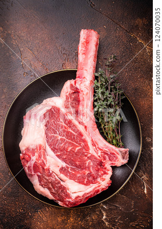 Fresh Tomahawk beef steak, raw marbled rib eye with bone on plate with herbs. brown background. top view Fresh Tomahawk beef steak, raw marbled rib eye with bone on plate with herbs. brown background. top view 124070035