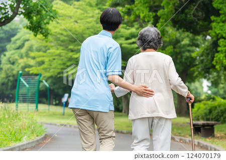 Rear view of a senior woman using a cane and her caregiver Rear view of a senior woman using a cane and her caregiver 124070179