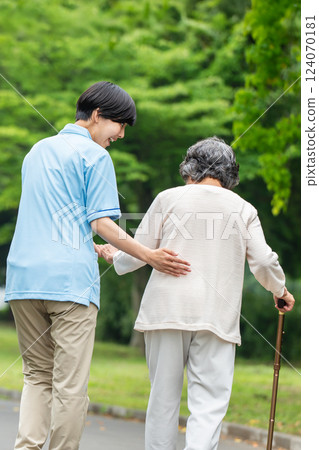 Rear view of a senior woman using a cane and her caregiver 124070181