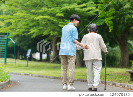 Rear view of a senior woman using a cane and her caregiver 124070183