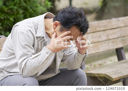 Middle-aged man holding his head in the park Middle-aged man holding his head in the park 124071010