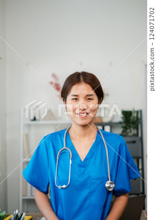 A cheerful healthcare worker in blue scrubs with a stethoscope, standing in a contemporary medical office environment. A cheerful healthcare worker in blue scrubs with a stethoscope, standing in a contemporary medical office environment. 124071702