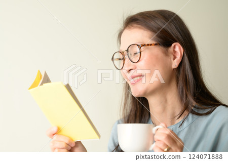 Senior woman with glasses enjoying reading a book with a cup of coffee 124071888