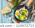 Spring scrambled eggs with green onions and bacon in a cast iron skillet on a rustic wooden background. Top view flat lay. 124072713