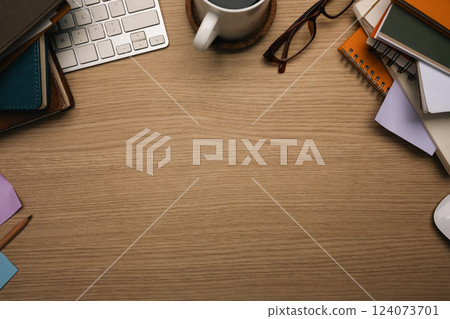 Top view of wooden desk with stacked books, a coffee cup, keyboard and glasses 124073701